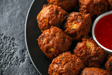 Indian Pakora snack spicy onion, red pepper with chilli sauce in a black plate