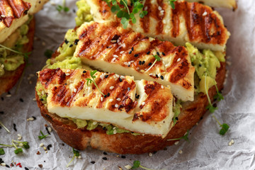 Avocado and grilled haloumi cheese toast with nigella and sesame seeds on crumpled paper. healthy breakfast