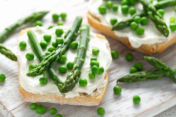 Appetizer bruschetta, toast with Asparagus, Peas and creamy soft cheese on white board. healthy food.