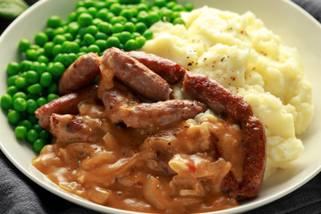 Mashed potatoes and sausages, bangers with onions gravy, green peas. close up