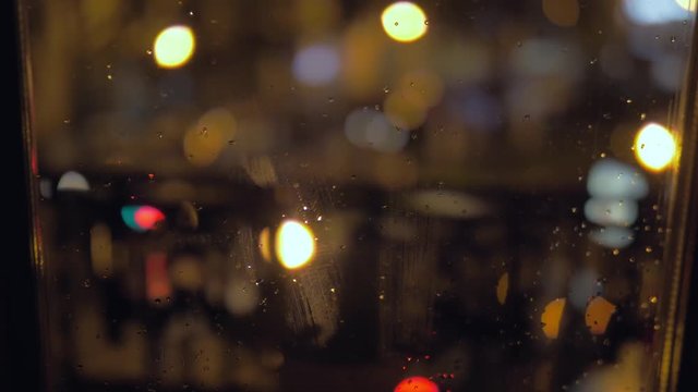 Close up shot of raindrops on a window on rainy day with blurred night city traffic as background