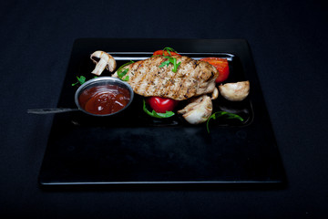 Chicken grill on the plate with tomatoes and mushrooms on a dark background