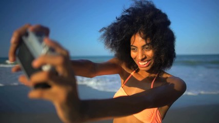 Young smiling African American female in swimwear having fun taking selfie on her beach holiday