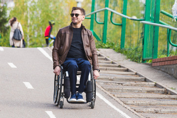 Fototapeta na wymiar A young man in a wheelchair rides along the park road.