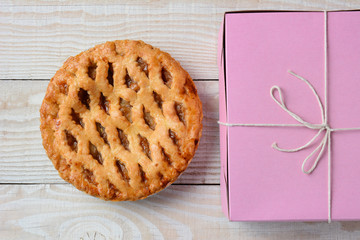 Fresh baked apple pie on a rustic white wood table next to a pink bakery box