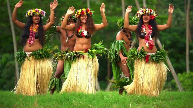 Polynesian men in warrior dress with girls in grass skirts and flower headdress dancing hula style while entertaining barefoot outdoors Tahiti French Polynesia 