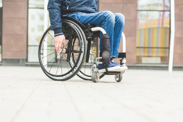 Young man in a wheelchair against the backdrop of a modern high-rise building.