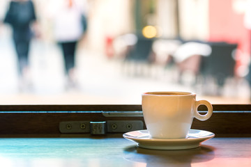 A cup of espresso coffee on a wooden table next to a window, indoors.