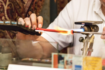 A jeweler artisan melting colored glass with a torch to make glass jewerly, Venice, Italy.
