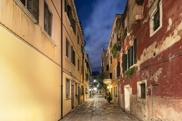 Fototapeta na wymiar A narrow street with apartments and a hotel signboard iluminated at night, Venice, Italy.