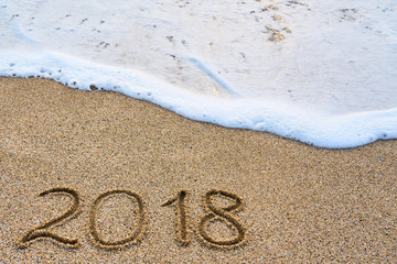 The year 2018 passed the concept. The wave of foam washes away the inscription 2018 written on the sand.  