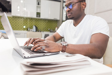 Young African American businessman working on a laptop in the kitchen in a modern interior.