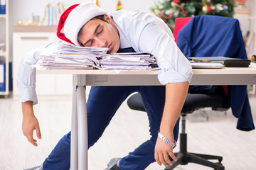 Young handsome employee celebrating Christmas at workplace 