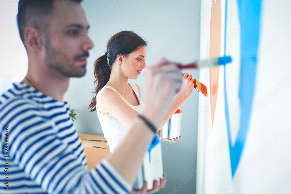 Wall mural Portrait of happy smiling young couple painting interior wall of new house. young couple