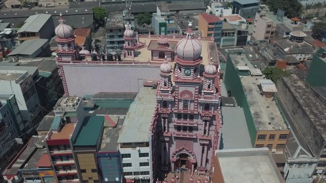 Aerial drone point of interest above the famous Red Mosque (Jami Ul-Alfar Mosque) in the capital city of Colombo, Sri Lanka surrounded by buildings, people walking and a bustling road in the sunshine