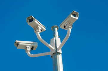 Three outdoor CCTV cameras against a clear blue sky