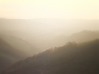a soft hillside tree covered valley landscape blurred by fog at sunrise glowing a warm orange color with the tops of hills showing though the mist
