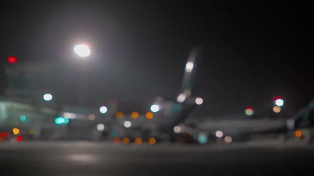 Wide blurred shot of a jet airplane standing near the airport terminal at night