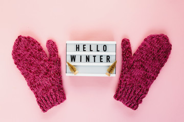 Warm, cozy winter clothing hat, mittens, lightbox and christmas decorations  as frame on pastel pink background. Christmas concept flat lay. Hello winter title