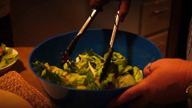 Slow Motion Close Up of woman tossing salad with tongs, warm indoor lighting