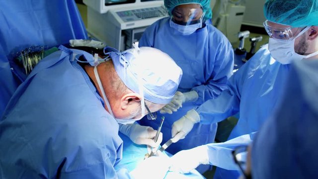 Medical multi ethnic hospital specialist team in scrubs training in the operating theatre in Orthopaedic surgery using tools and modern electronic monitors 