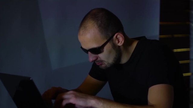 A man hacker in sunglasses in a dark room works with the program code. concept on cybercrime
