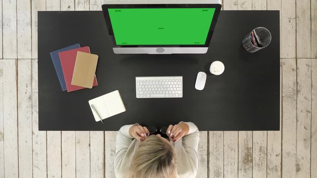 Woman putting glasses on while using computer. Green Screen Mock-up Display.