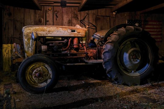 A vintage or antique tractor in an old dimly lit barn at nighttime