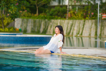 outdoors lifestyle portrait of young happy and beautiful Asian Chinese tourist woman relaxing at tropical resort swimming pool enjoying Summer holidays smiling cheerful