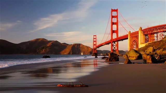 Panning view of the Golden Gate Bridge and the Pacific Ocean from the hidden and secluded rocky Marshall's Beach at sunset in San Francisco, California