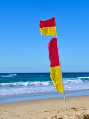 Yellow and red lifesaving flags on a Queensland beach on a windy day with ocean waves in the background
