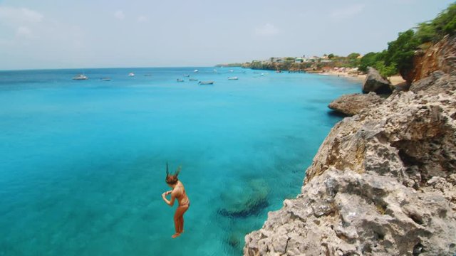 Slow Motion Young woman cliff jumping in tropical Caribbean Sea on Curacao Beach