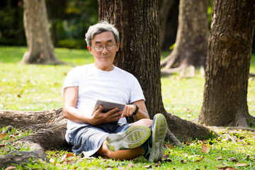 Naklejka na ściany i meble Elderly man use the tablet sitting in the park