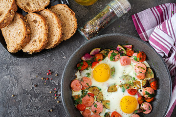 Frying pan with tasty cooked egg, sausages and vegetables on grey table. Breakfast. Top view