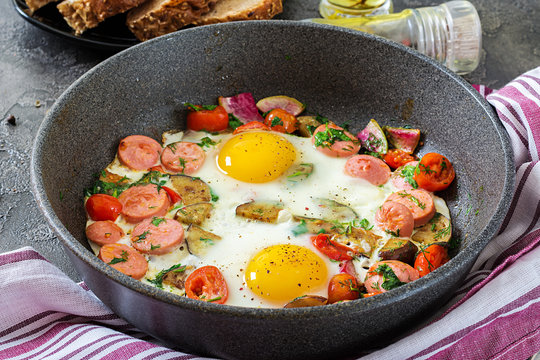 Frying pan with tasty cooked egg, sausages and vegetables on grey table. Breakfast.