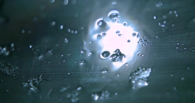 Ice shards and snowflakes slide down a wet window during a winters night. It is dark out, a street lamp illuminates the crystals.