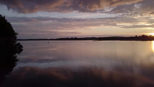 Rising drone over Scenic Swedish lake called Levrasj&radic;&part;n in Brom&radic;&part;lla during a beautiful sunset on a warm summer evening at the lake in Sk&radic;&bull;ne Sweden. Reflections of the sky in the water as boat approach