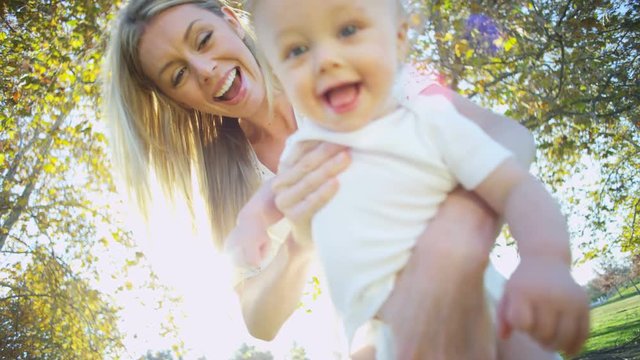Portrait of smiling attractive blonde young European mother having fun with her baby son outdoors in the sunshine 