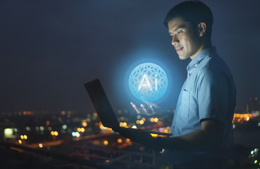 Businessman stand on roof top using laptop with hold the (AI)Artificial intelligence hologram,smart city and network connect concept