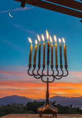 Menorah with burning candles is traditional symbol for Hebrew Holidays and celebration of Hanukkah. Background of night or dawn sky, selective focus on menorah © sergei_fish13