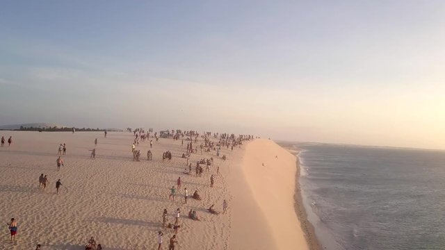 Drone flying over beachgoers tourists on a sand dune in Jericoacoara, Brazil