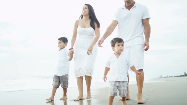 Young ethnic Latino family happy walking along the beach together by the coast 