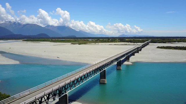 Aerial view of road bridge across the blue river with mountain scenery in summer of West Coast in South island, New Zealand. 4K video taken from drone.