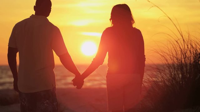 Silhouette of loving young African American couple holding hands and enjoying sunrise on beach holiday RED EPIC