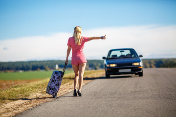 young woman hitch-hiking on a road at the fields