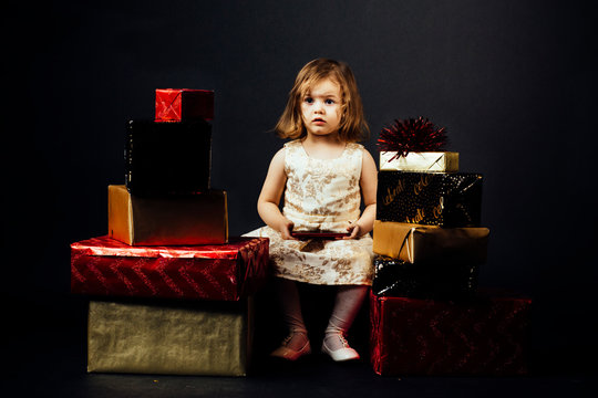 Portrait of a small toddler girl surrounded with gifts, isolated on black studio background