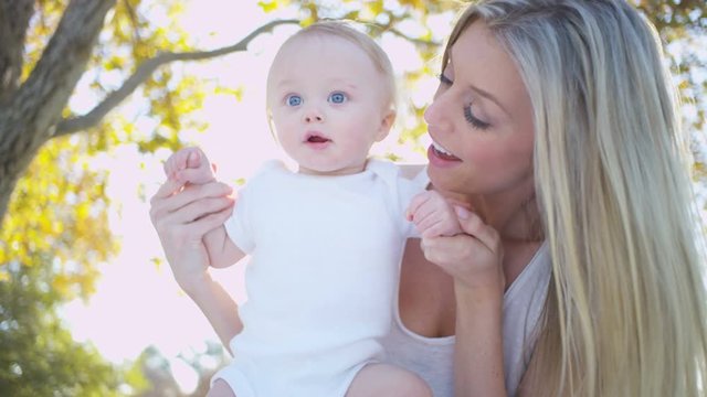 Loving cute blonde Caucasian mother with her young baby boy outdoors in the park 