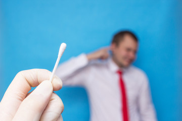 ear plug in the ear of a young man, the doctor holds in his hand a remedy for earwax, a cotton swab