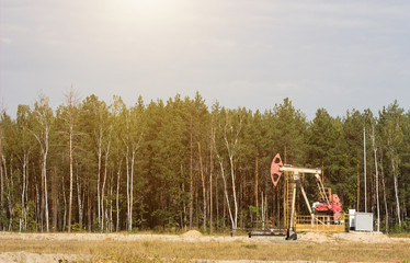 Obraz na płótnie Canvas Oil well for the extraction of oil and gasoline and gas on the background of the forest, the production of fuel-combustible and petroleum substances, the extraction of petroleum products, copy-space