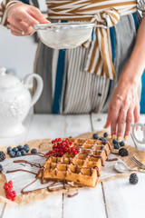 Woman serving sweet waffles with berries and chocolate